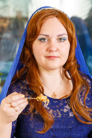 A Jewish woman with her head covered in a blue cape at the Passover Seder table eats haroset.の写真素材