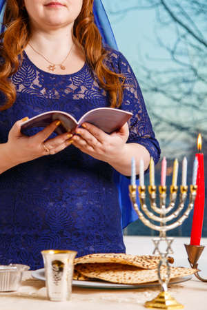 A Jewish woman with her head covered in a blue cape at the Passover Seder table reads the Passover Haggadah.の写真素材