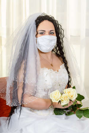 A Jewish bride sits waist-deep in a synagogue before a chuppa ceremony during a pandemic, wearing a medical mask and a bouquet of flowers, awaits the groom.の写真素材