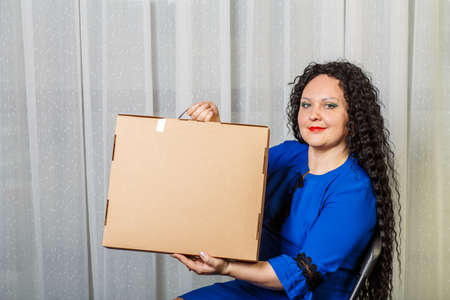 Curly joyful brunette woman holds in her hands a long-awaited purchase shows her.の写真素材