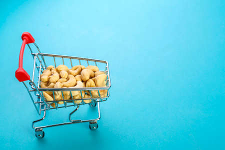 Food cart filled with peeled cashews on a blue background. Copy space. Horizontal photoの写真素材
