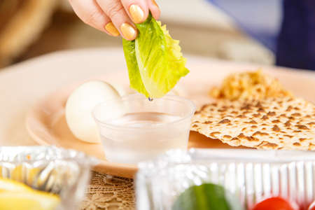 A woman's hand at the Easter Seder table dips maror and karpas in salt water. Horizontal photoの写真素材