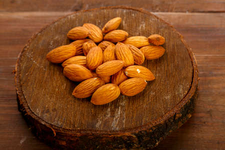 Almond nuts scattered on a round board on a wooden table. Horizontal photoの写真素材