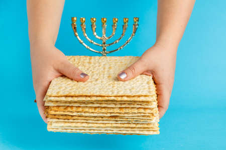 A stack of matzo in female hands on a blue background near the menorah. Horizontal photoの写真素材