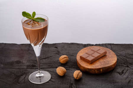 Chocolate cocktail with nuts and mint in a glass near chocolate and nuts on a black background....