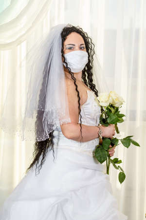A Jewish bride in a synagogue before a chuppa ceremony during a pandemic, wearing a medical mask and a bouquet of flowers.の写真素材