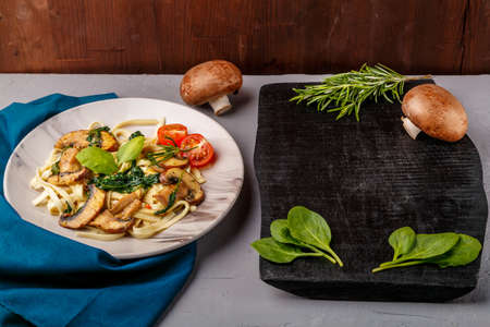Udon with mushrooms and spinach in a plate on a blue napkin on a concrete background near greens. horizontal photoの写真素材