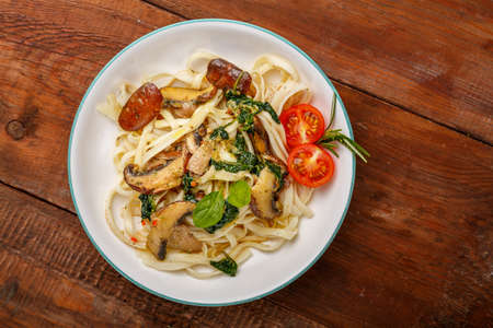 Udon with mushrooms and spina horizontal photoch and cherry tomatoes in a plate on a wooden table.の写真素材