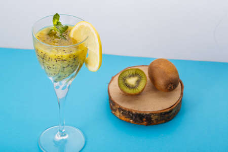 Kiwi smoothie garnished with mint and lemon in a glass on a blue background near kiwi. Horizontal photoの写真素材