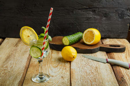 Cocktail cucumber water with lemon and mint in a glass on a wooden table on a black background near lemon and cucumber. Horizontal photoの写真素材