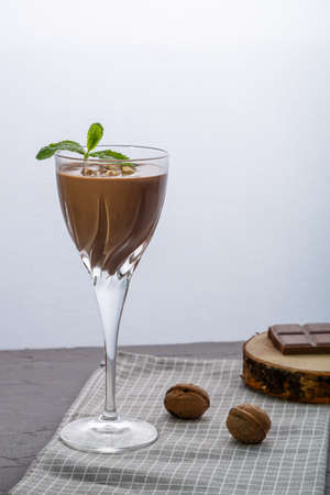 Chocolate cocktail with nuts and mint in a glass on a blue background near nuts and chocolate on a napkin. Vertical photoの写真素材