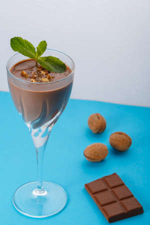 Chocolate cocktail with nuts and mint in a glass on a blue background near nuts and chocolate. Vertical photoの写真素材