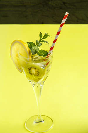 Kiwi cocktail decorated with lemon and mint in a glass on a napkin on a yellow background. Vertical photoの写真素材
