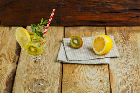 Cocktail with kiwi mint and lemon in a glass on a wooden table next to lemon and kiwi on a napkin. Horizontal photoの写真素材