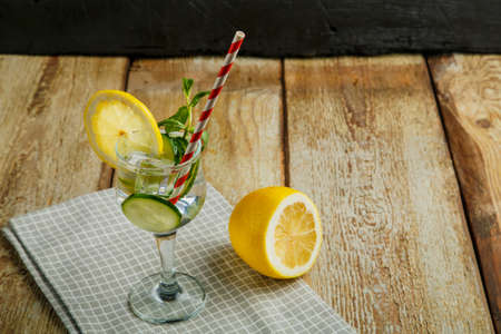 Cocktail cucumber water with lemon and mint in a glass on a napkin on a black background near lemon and cucumber.の写真素材