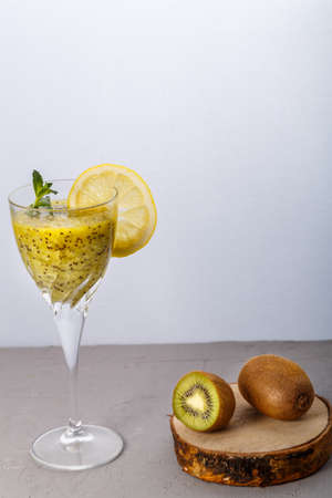 Kiwi smoothie garnished with mint and lemon in a glass on a gray background near kiwi. Vertical photoの写真素材