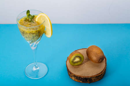 Kiwi smoothie garnished with mint and lemon in a glass on a blue background near kiwi. Horizontal photoの写真素材