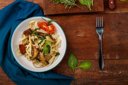 Udon with mushrooms and spinach in a plate on a blue napkin next to a fork and mushrooms. Horizontal photoの写真素材