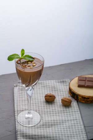 Chocolate cocktail with nuts and mint in a glass on a blue background near nuts and chocolate on a napkin. Vertical photoの写真素材