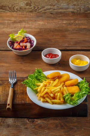 French fries with chicken nuggets next to cheese sauce and ketchup in a gravy boat on wooden planks. Vertical photoの写真素材