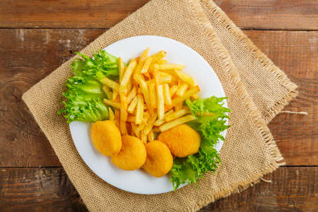 French fries with chicken nuggets in a plate with salad on a wooden table on a linen napkin....