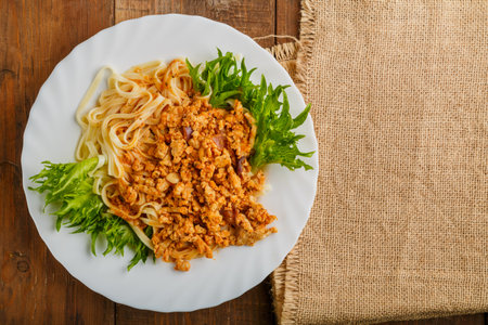 A plate of bolognese pasta decorated with herbs on a wooden table next to a linen napkin. Horizontal photoの写真素材