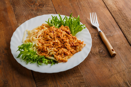 A plate of bolognese pasta decorated with herbs on a wooden table next to a fork. Horizontal photoの写真素材