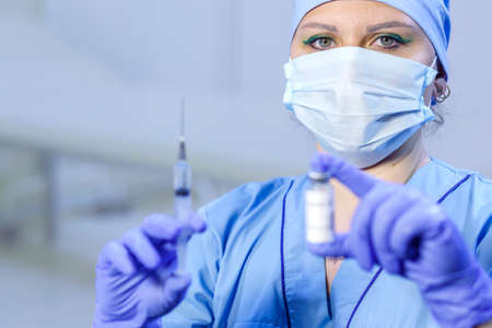 A doctor in medical gloves and a mask holds a vial with a vaccine and a syringe. Horizontal photoの写真素材