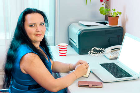 Brunette woman at home office working on laptop while looking at camera. Horizontal photoの写真素材