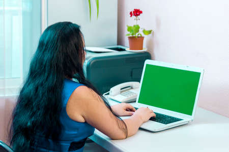 A brunette woman in a home office works with a laptop to the green screen camera. Horizontal photoの写真素材