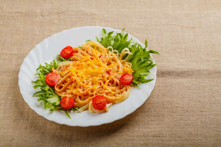 A plate of pasta with cherry tomatoes and cheese on a linen tablecloth. Horizontal photoの写真素材