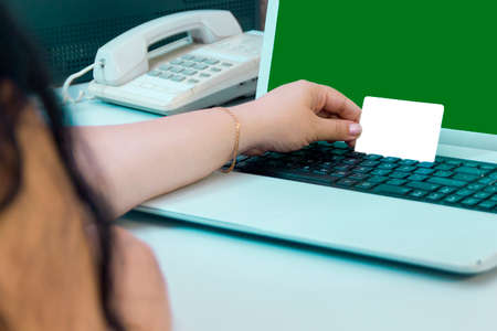 A female hand holds a bank card when paying for purchases online green screen. Horizontal photoの写真素材