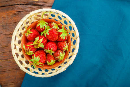 Fresh strawberries in a wicker plate on a blue napkin on a wooden background.の写真素材