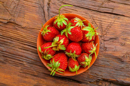 Ripe strawberries in a clay plate on a dark wooden surface. Horizontal photoの写真素材
