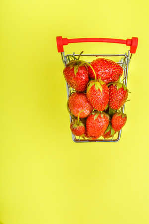 ripe strawberries in a grocery cart on a yellow background. Vertical photoの写真素材