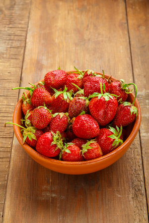 Fresh large strawberries in a clay plate on a wooden table. Vertical photoの写真素材