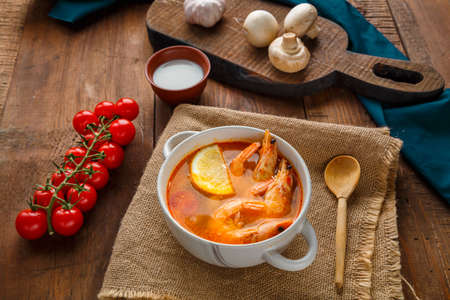 Tom yam soup with shrimps and coconut milk on a table on a napkin next to coconut milk mushrooms and tomatoes. Horizontal photoの写真素材