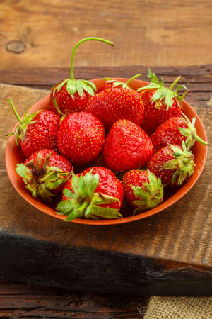Fresh large strawberries in a clay plate on a wooden table on a stand. Vertical photoの写真素材