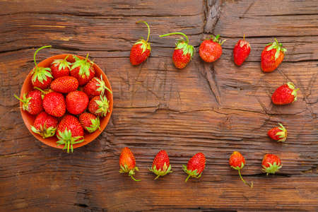 Ripe strawberries in a plate on a wooden table next to a frame. Horizontal photoの写真素材