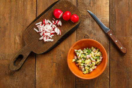 Salad in a clay plate on a table on a wooden table next to a radish on planks and a knife. Horizontal photoの写真素材