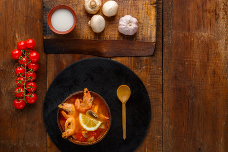 Tom yam soup with shrimps and coconut milk on the table on a round board near milk mushrooms and tomatoes. Horizontal photoの写真素材