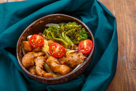 Udon with meat and vegetables in yakiniku sauce in a plate of coconut shells on a wooden table on a blue napkin. Horizontal photoの写真素材