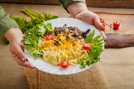 A plate of pasta with mushrooms and cheese in female hands. Horizontal photoの写真素材
