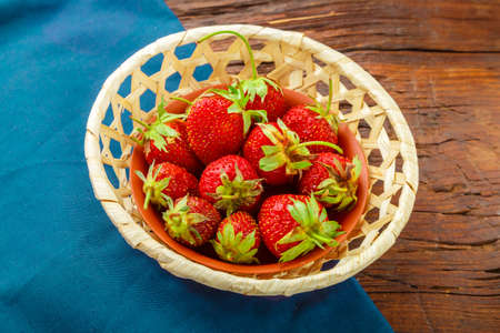Fresh strawberries in a wicker plate on a blue napkin on a wooden background. Horizontal photoの写真素材