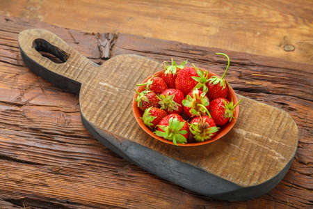 Fresh strawberries in a plate on a wooden board on a wooden background. Horizontal photoの写真素材