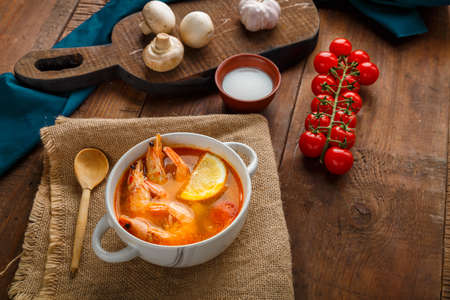 Tom yam soup with shrimps and coconut milk on a table on a napkin next to coconut milk mushrooms and tomatoes. Horizontal photoの写真素材