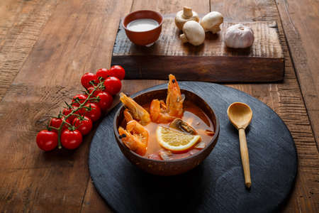 Tom yam soup with shrimps and coconut milk on the table on a round board near milk and a wooden spoon. Horizontal photoの写真素材