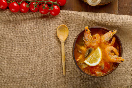 Tom yam soup with shrimps and coconut milk on the table on a napkin next to the ingredients and a wooden spoon. copy space. Horizontal photoの写真素材