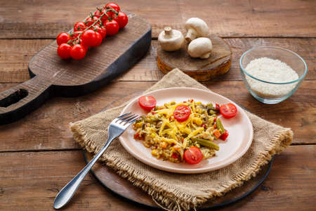 Risotto with beefs and cheese in a plate on a wooden background on a napkin next to rice mushrooms and tomatoes on planks. Horizontal photoの写真素材