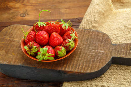 Ripe strawberries in a plate on a wooden table on a wooden board.の写真素材